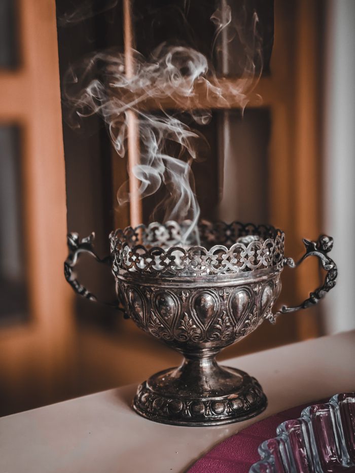 Ornate antique metal incense burner with swirling smoke indoors.